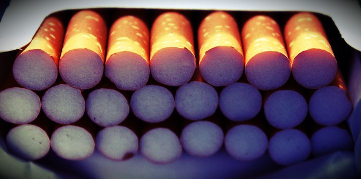 An open pack of cigarettes, filters lit orange from behind
